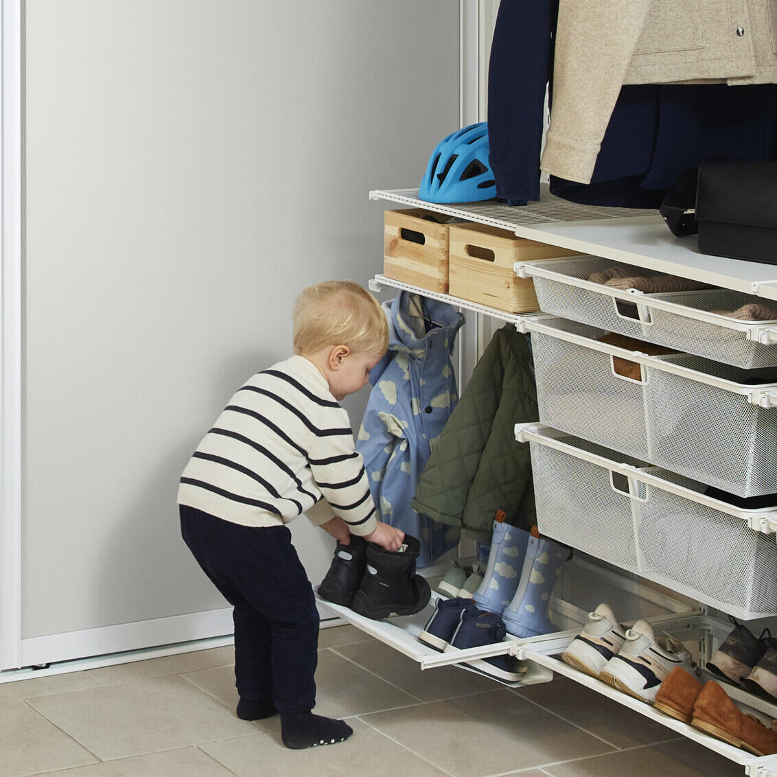 Pieni poika laittaa saappaat takaisin Classic by Elfa -säilytyskalusteeseen.