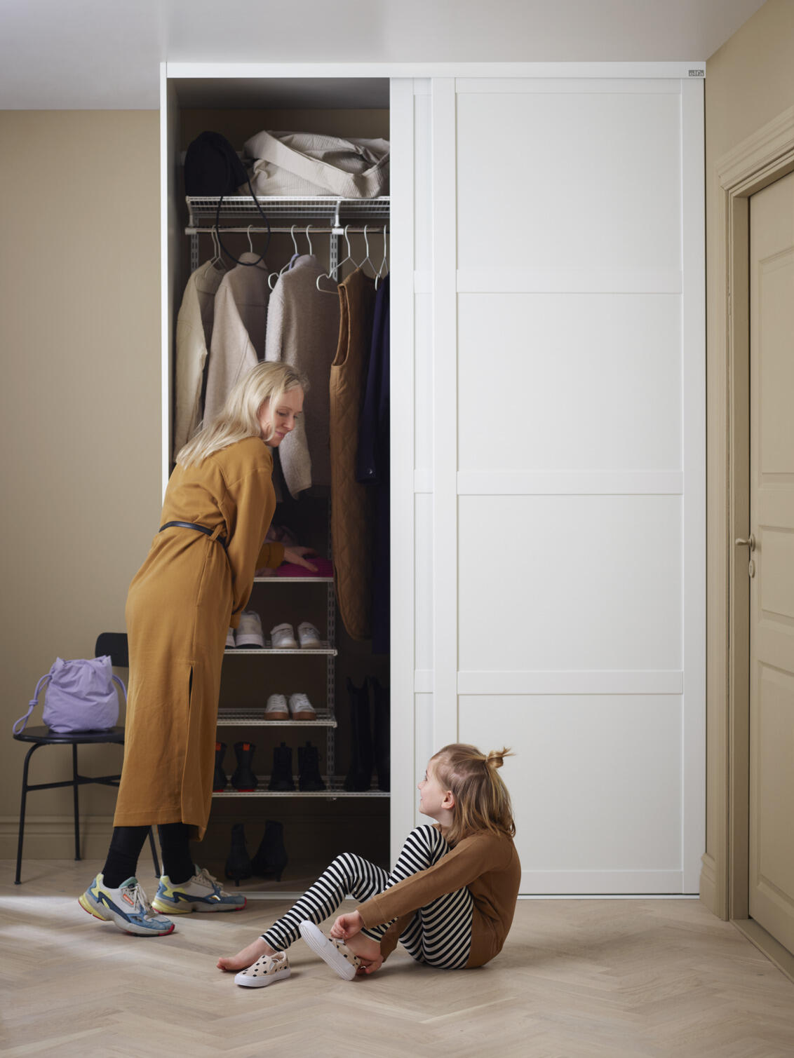 Nainen ja tyttö Classic by Elfa -eteisvaatekaapissa, jossa on valkoiset Grace-liukuovet.
