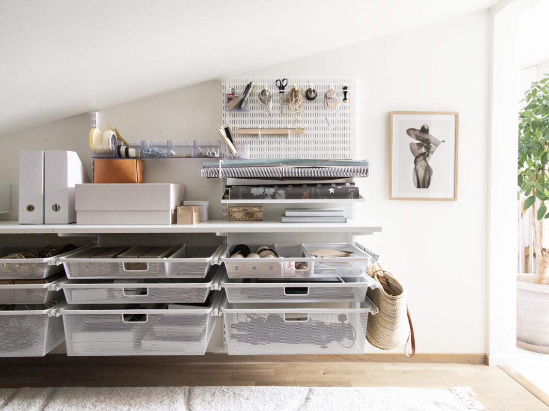 Viistokattoinen askarteluhuone, jossa on Classic by Elfa -säilytyskalusteita. Askartelutarvikkeet säilytetään koreissa ja säilytystaululla.