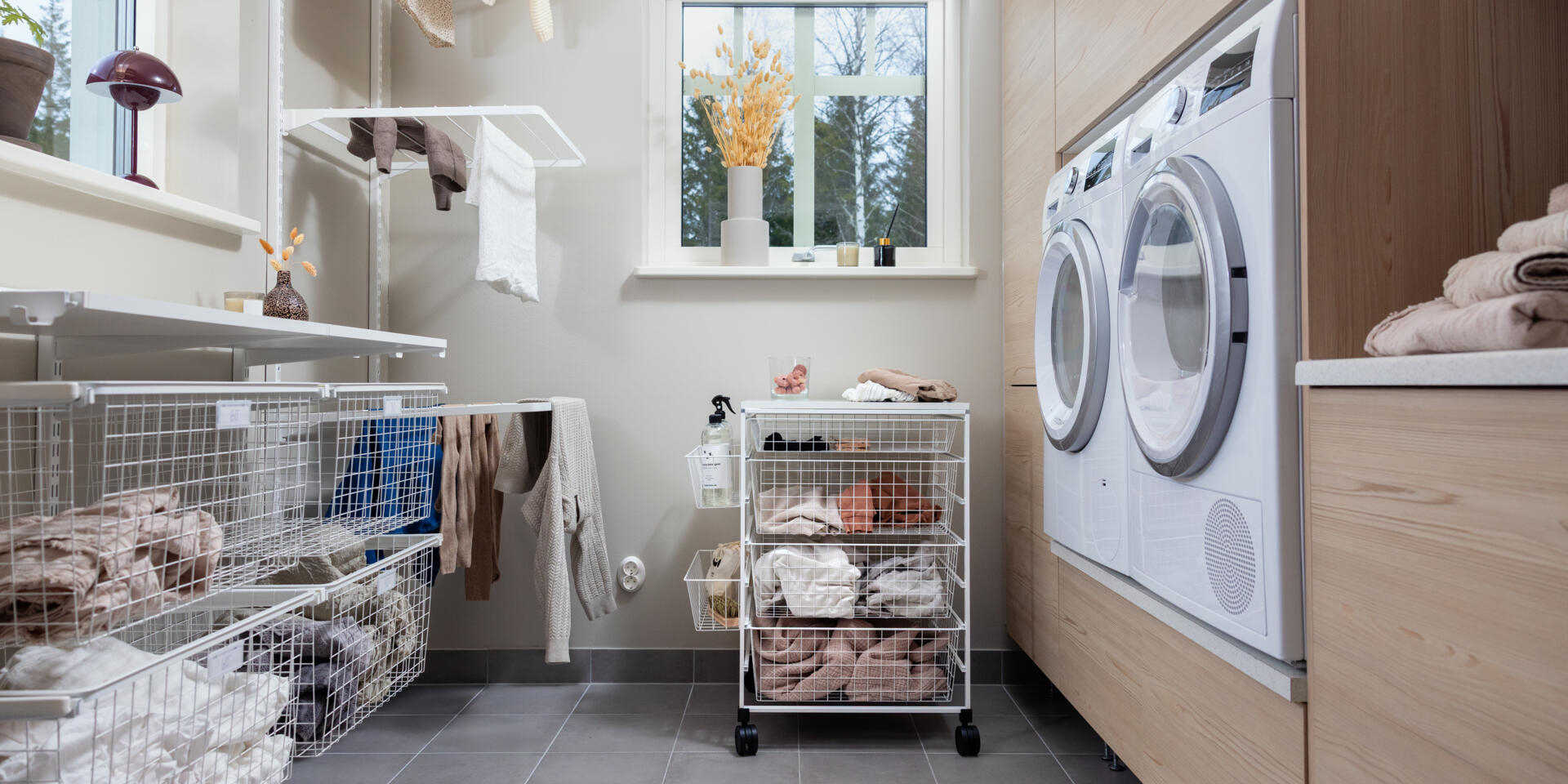 Pesuhuone, jossa on seinälle ripustettava Classic by Elfa -säilytyskaluste ja pyörillä varustettu kori.