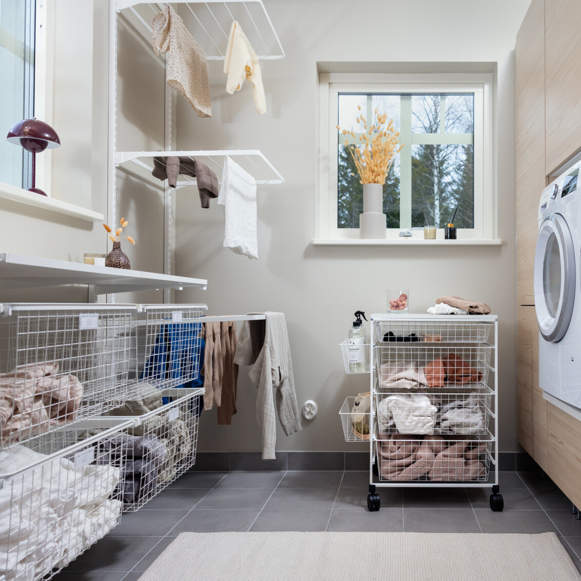 Pesuhuone, jossa on seinälle ripustettava Classic by Elfa -säilytyskaluste ja pyörillä varustettu kori.