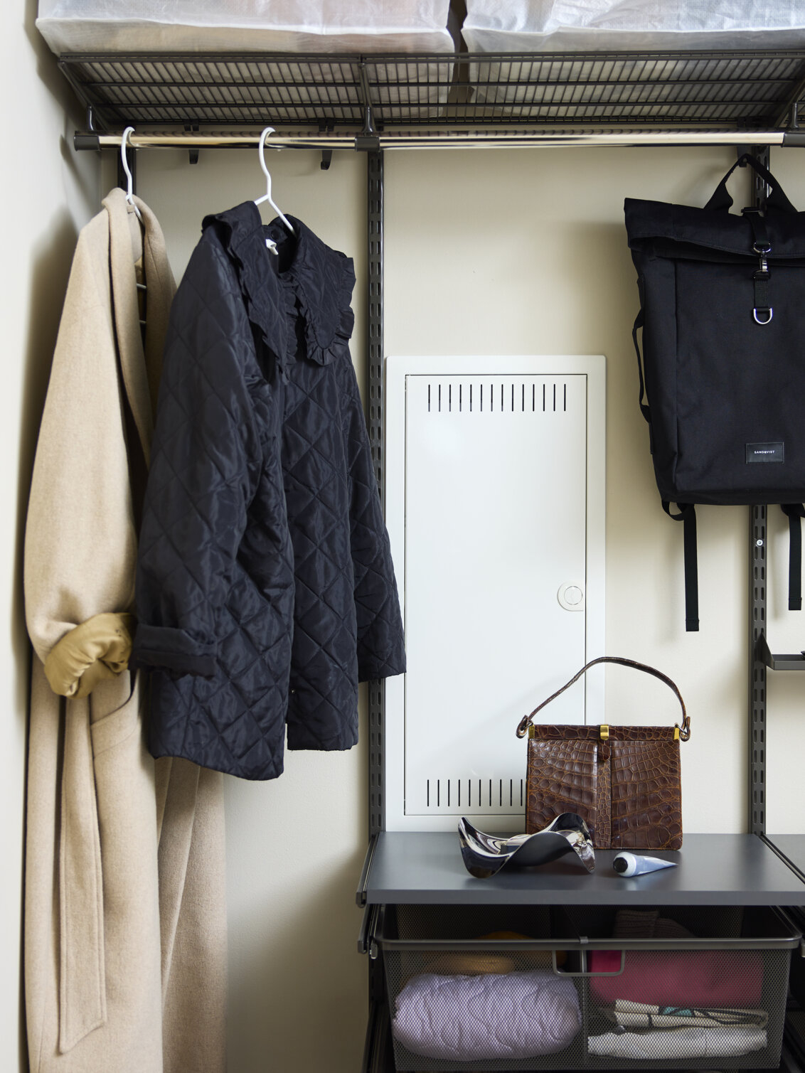 Garderob från Classic by Elfa i grått med ytterkläder och väskor där förvaringen är byggd runt ett elskåp.