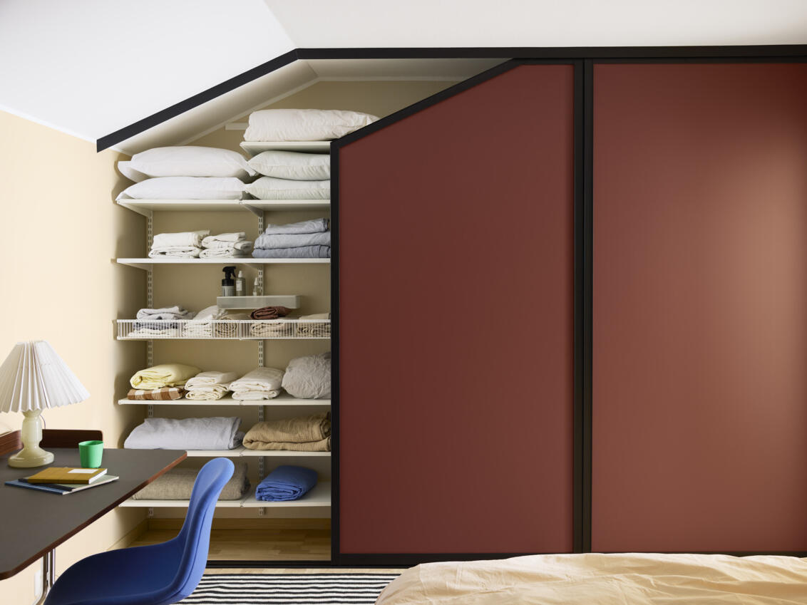 Sypialnia z szafą z bordowymi drzwiami przesuwnymi Elfa pod skośnym sufitem.