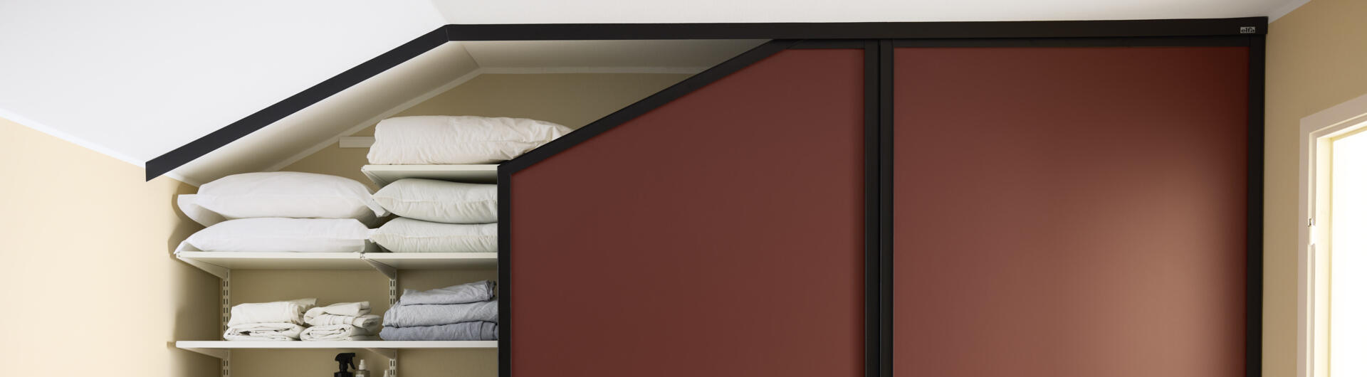 Soverom med garderobe som har vinrøde skyvedører fra Elfa, under skråtak.