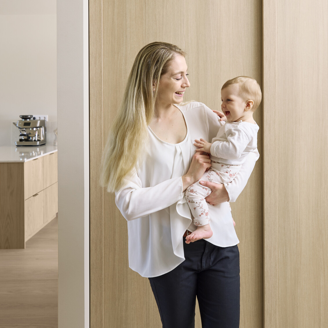 En mamma håller sitt barn i hallen framför en garderob från Elfa med skjutdörrarna Artic.