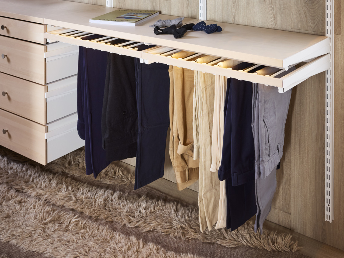 Porte-pantalons coulissant Décor+ d’Elfa sur lequel sont suspendus des pantalons de couleurs neutres.