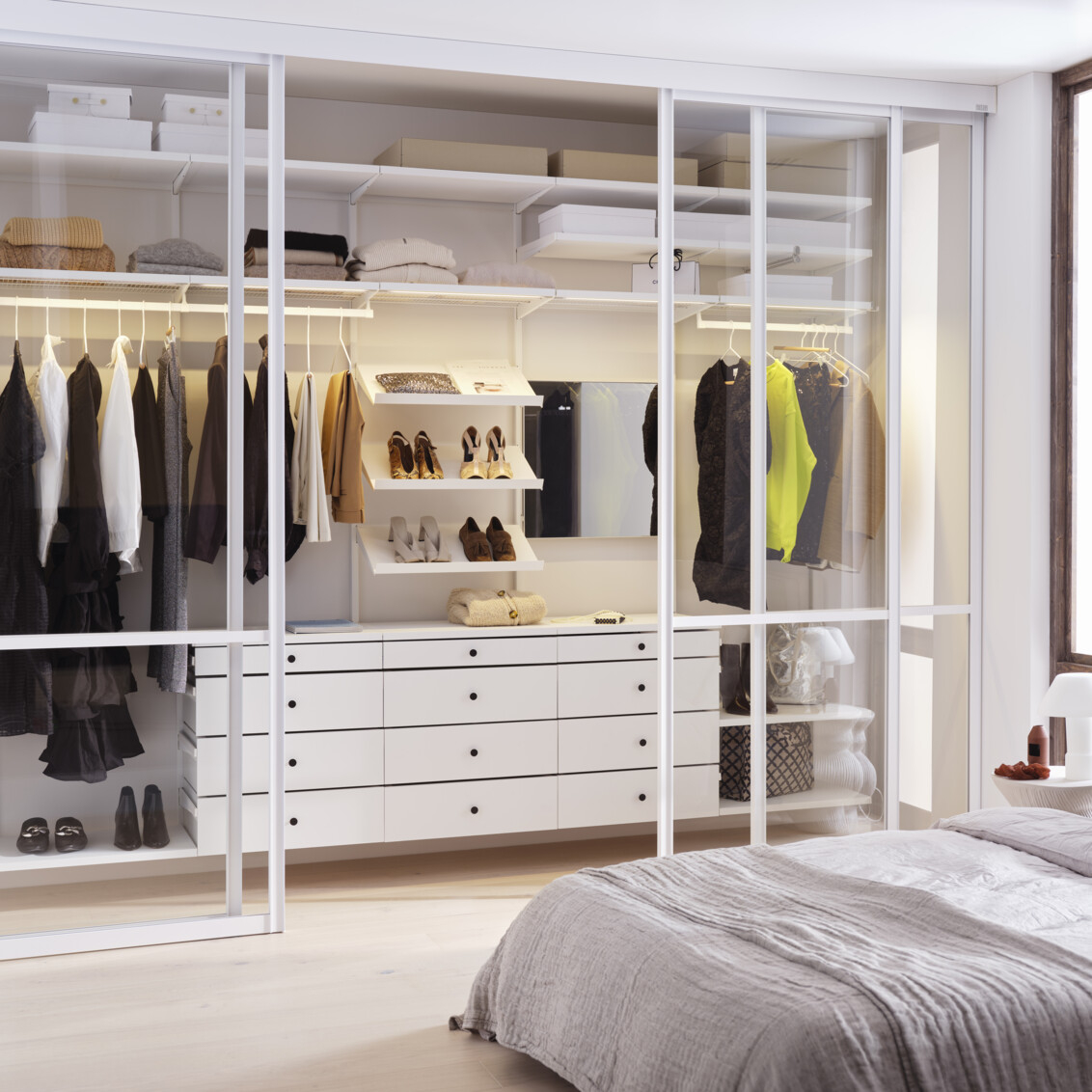Slaapkamer met Décor+ by Elfa garderobe in wit met uittrekbare laden en glazen schuifdeuren.