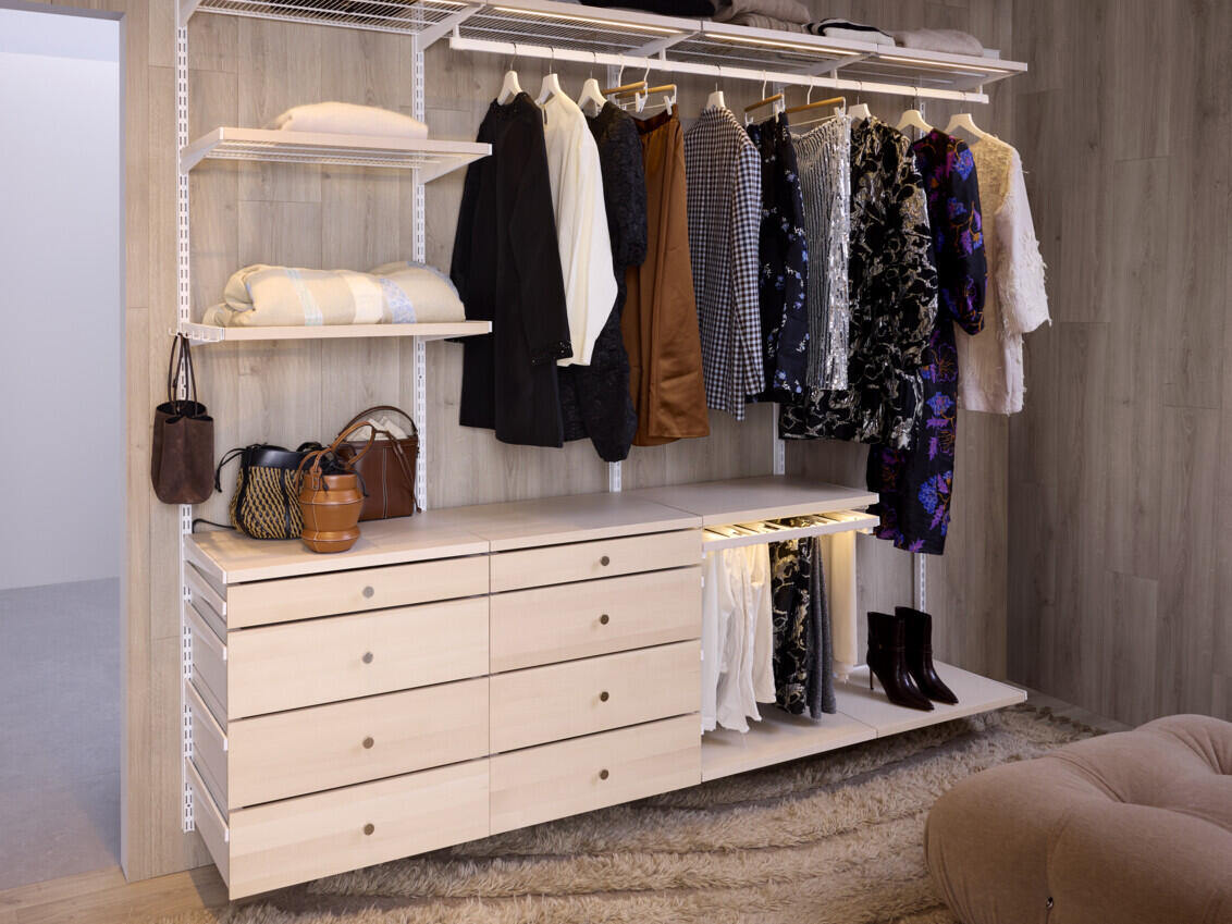Biała otwarta szafa Décor+ marki Elfa z drucianymi półkami, wieszakami na ubrania, wieszakami na spodnie i szufladami z brzozy.