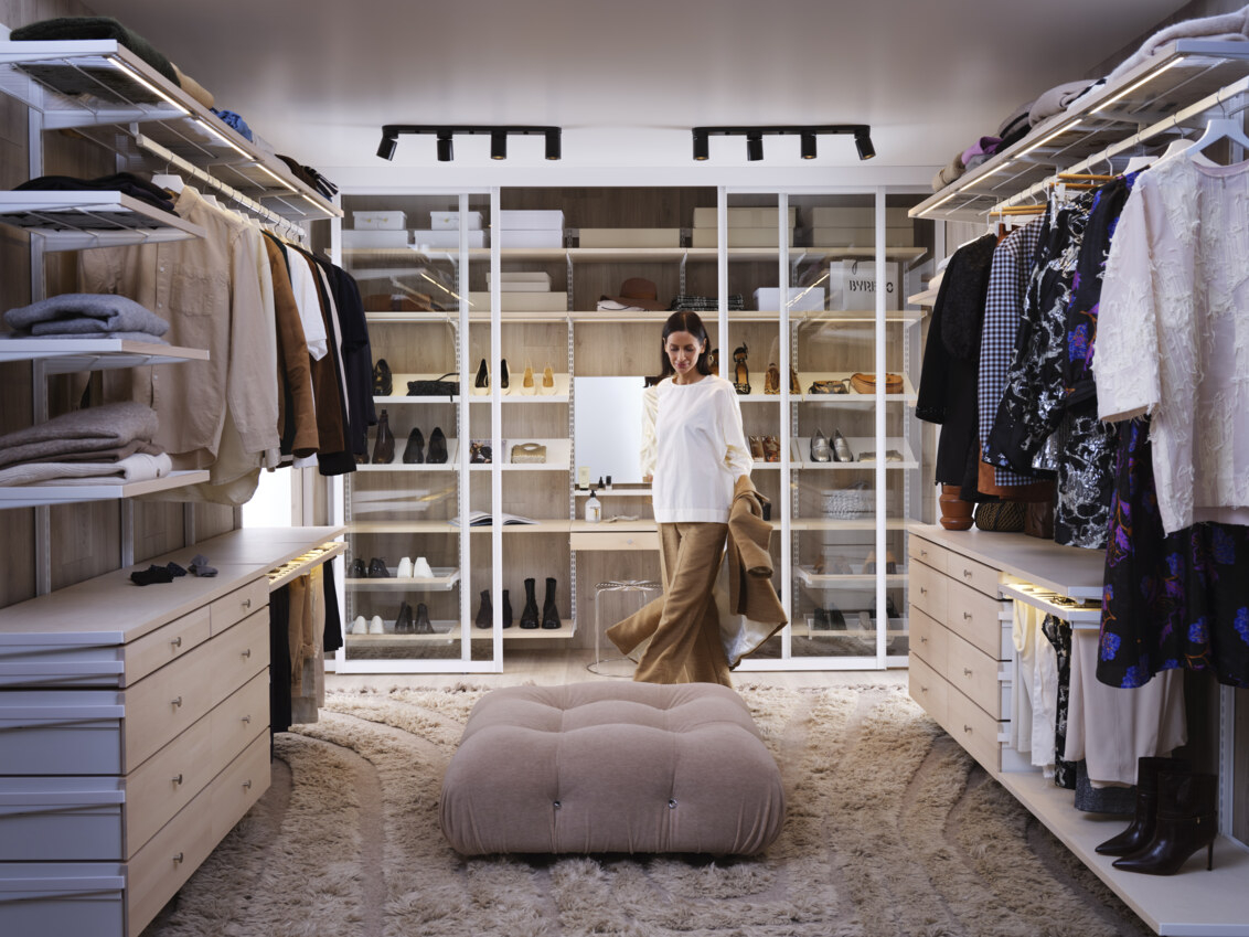 Nainen pitää takkia keskellä walk-in-closetia, jossa on valkoinen ja koivuinen Décor+-vaatesäilytyskaluste Elfalta.