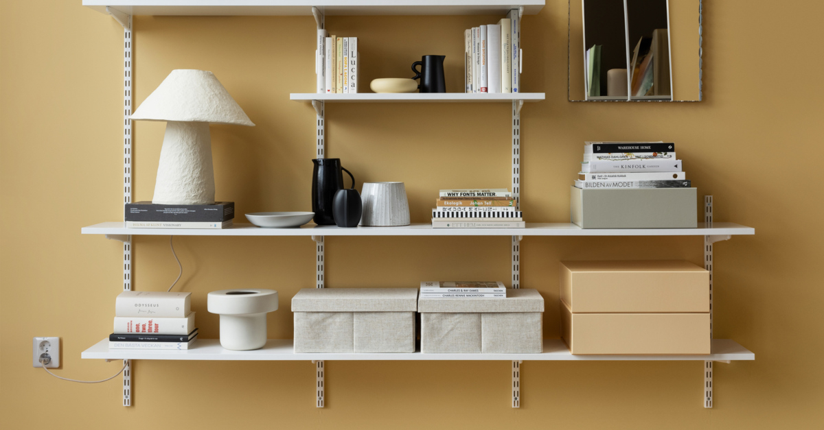 Librería con largueros de Elfa en blanco con libros, cajas de almacenamiento y artículos decorativos.