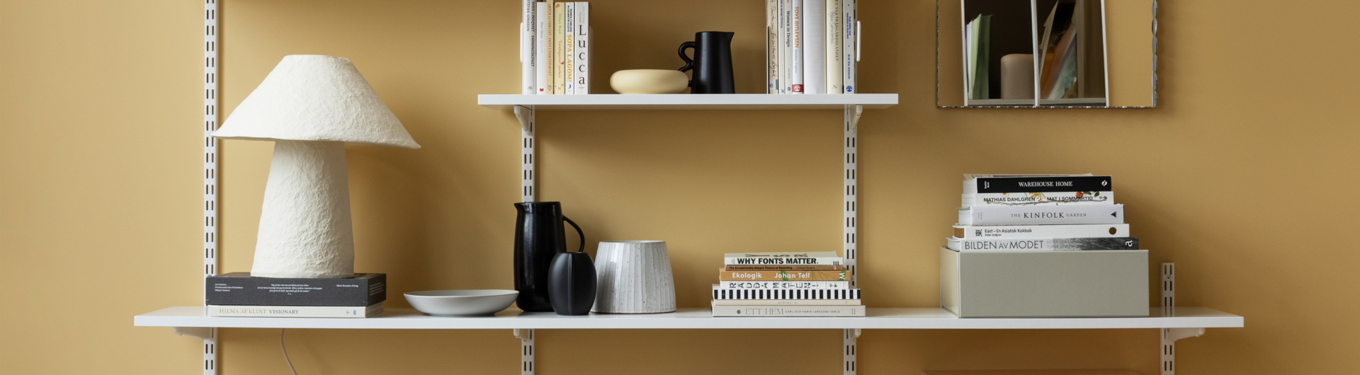 Librería con largueros de Elfa en blanco con libros, jarrones y otros artículos decorativos.