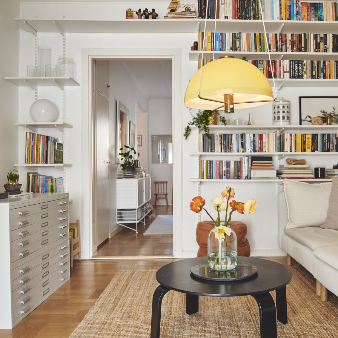 Vardagsrum med Sparring by Elfa bokhylla i vitt som omger dörröpningen.