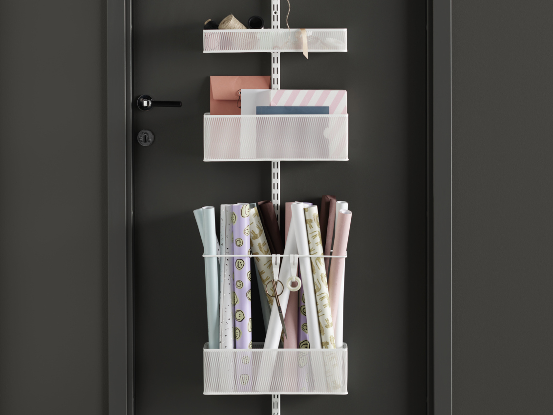 Valkoinen Classic by Elfa -ovisäilytyskaluste mustalla ovella, verkkokorit, joissa on kirjoitustarvikkeita ja lahjapaperia.