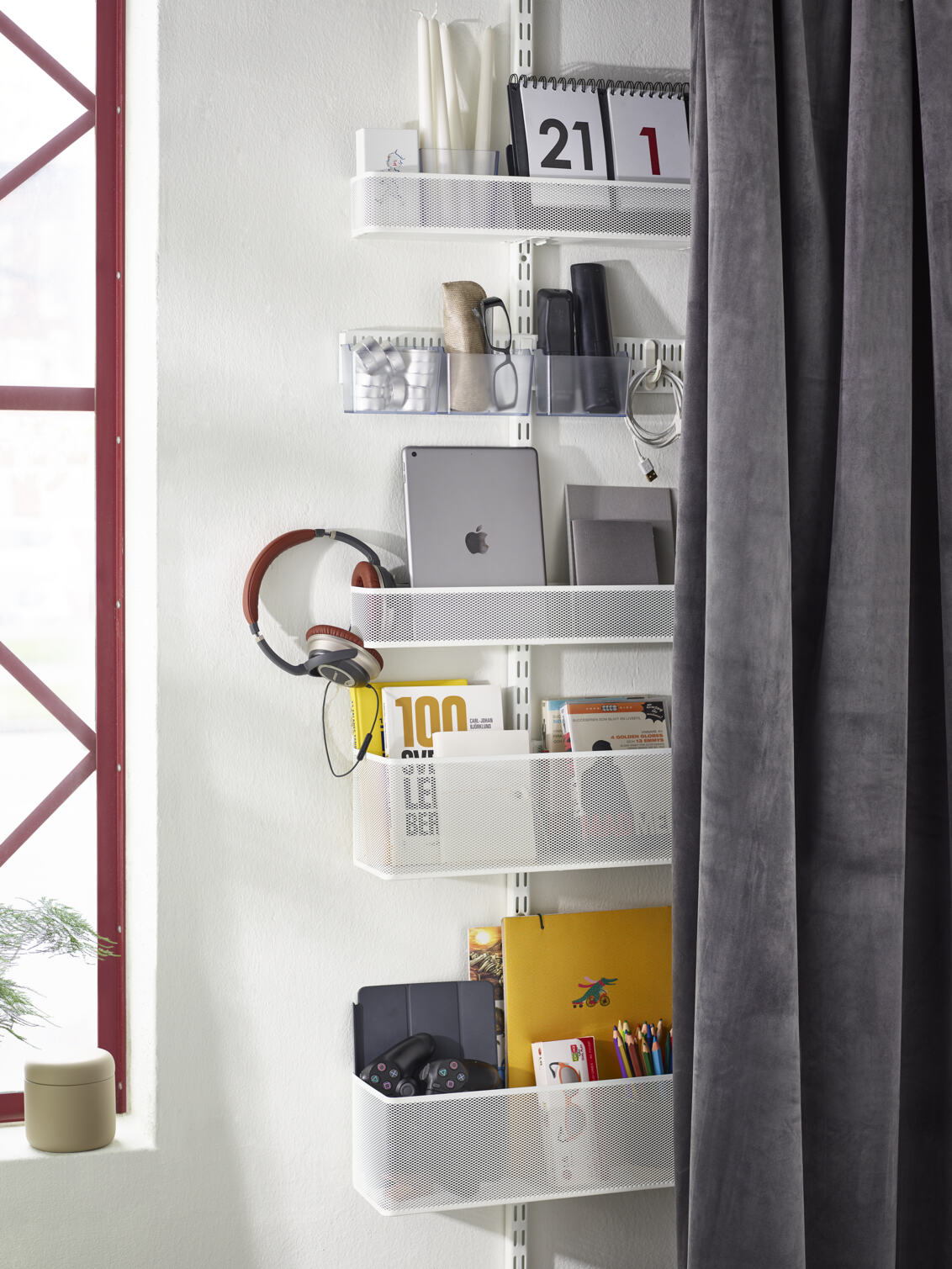 Classic by Elfa förvaring bakom en gardin med meshkorgar som innehåller teknikprylar och böcker.