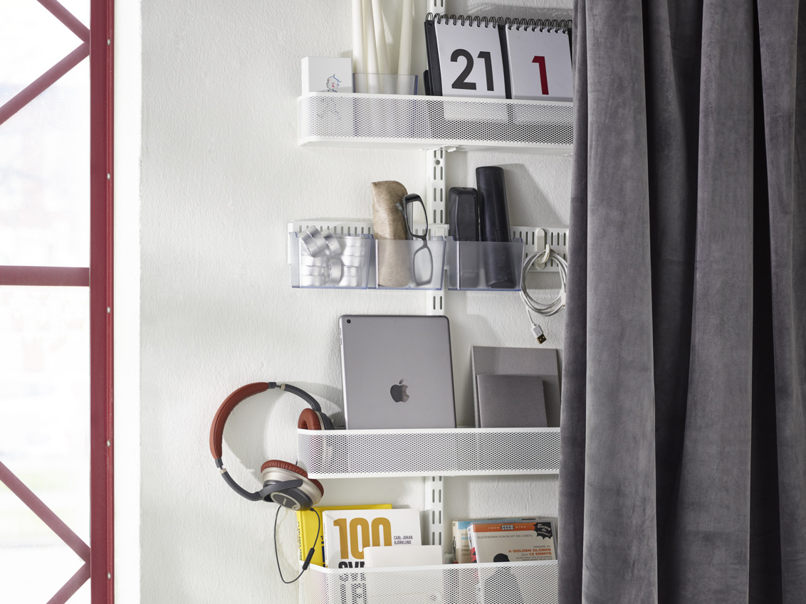 Classic by Elfa -säilytyskaluste verkkokoreilla varustetun verhon takana, jossa on teknisiä tavaroita ja kirjoja.