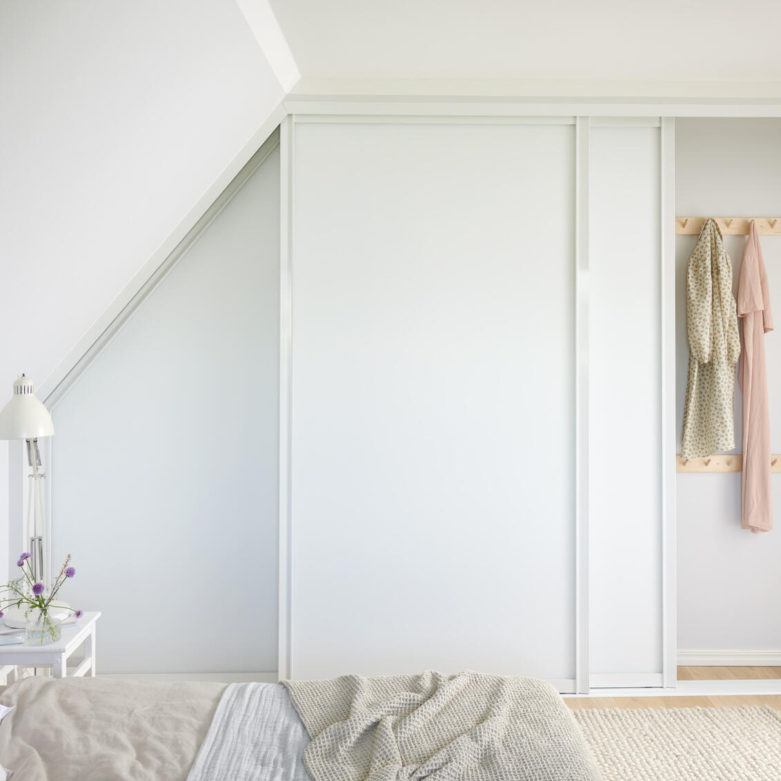 Soverom med Elfa garderobe med skyvedører i hvitt under skråtak.
