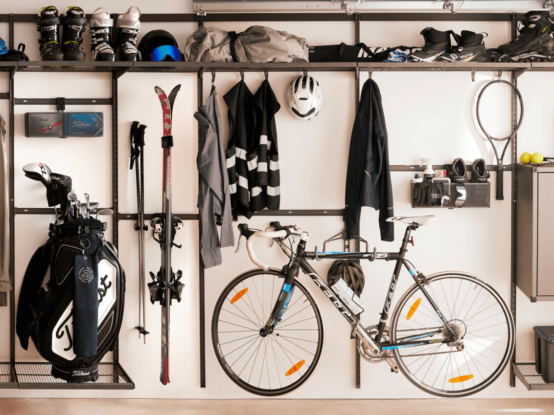 Garage med Garage+ by Elfa förvaring där det hänger golfutrustning, skidor och en cykel.