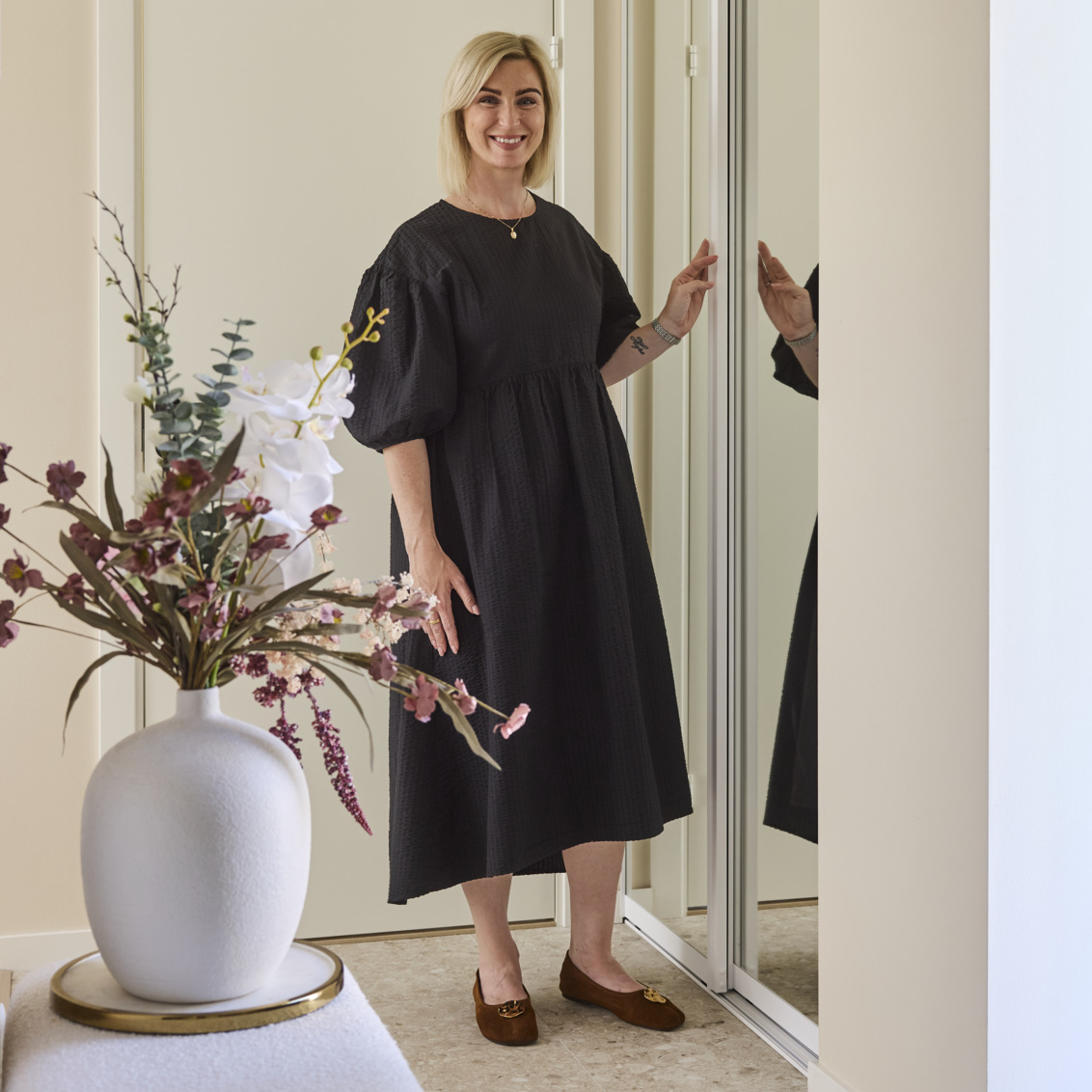 Frida Swanson står i en hall med en Elfa garderob som har skjutdörrar med spegel.