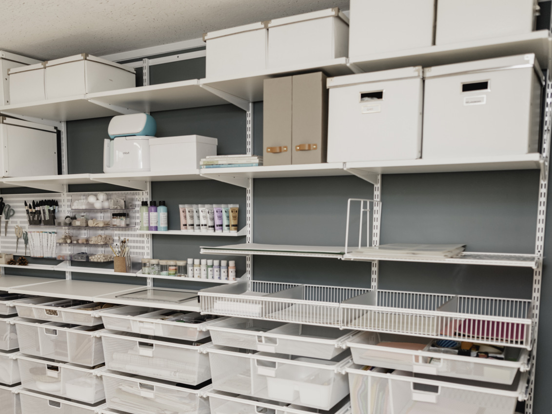 Askarteluhuone, jossa on Classic by Elfa -säilytyskalusteet valkoisina, hyllyjä, verkkokoreja, lankakoreja ja säilytystauluja.