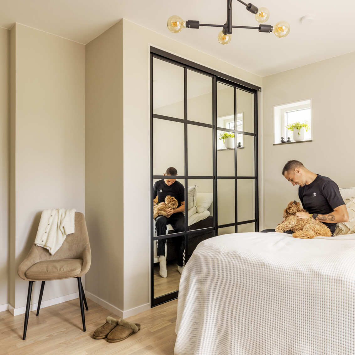 Sypialnia, w której Thobias Montler bawi się ze swoim psem przy szafie firmy Elfa z przesuwanymi drzwiami Artic z lustrzanym wypełnieniem.